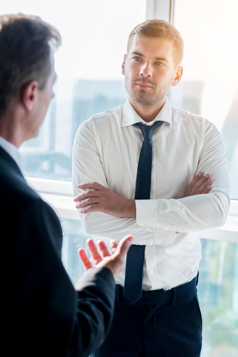 Un jeune professionnel en chemise et cravate écoute attentivement son interlocuteur lors d'un échange en entreprise